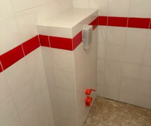 Pièce carrelée en blanc avec bande rouge avant installation des sanitaires – NATB